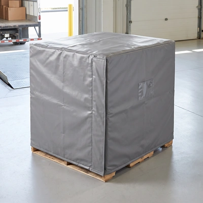 Gray insulated vinyl pallet cover fitted over a loaded pallet on a warehouse floor near a loading dock