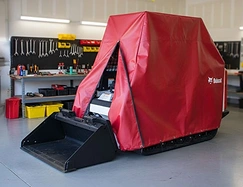 Red vinyl cover over a skid steer loader parked in a workshop